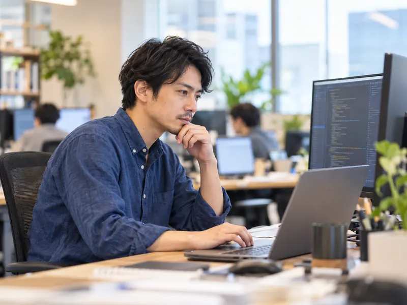 コードエディタが表示されたディスプレイで開発するエンジニア